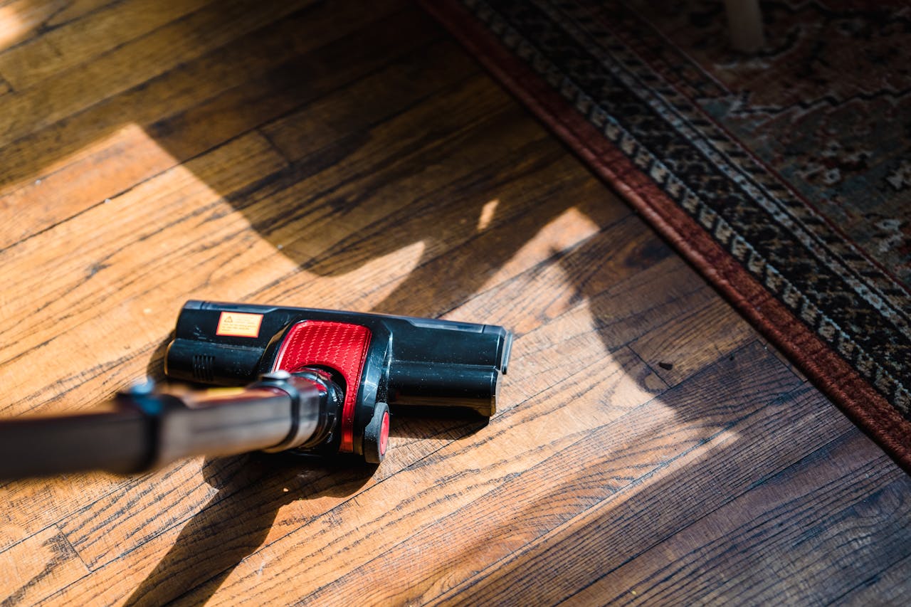 services-02 Close-up of a vacuum cleaner on wooden flooring near a patterned rug, showcasing domestic cleaning.