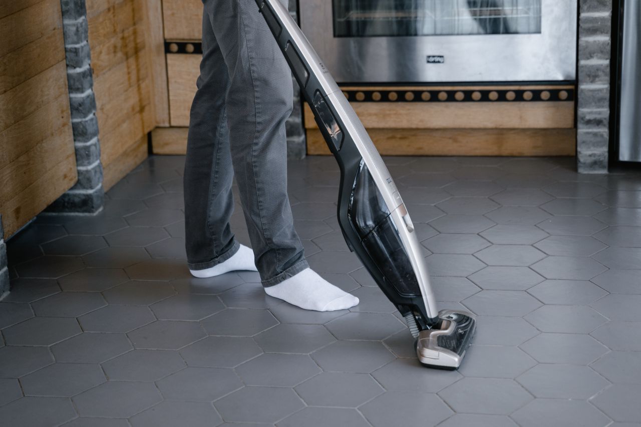 hero-img-01 A person cleaning a tiled floor with a modern vacuum cleaner indoors.
