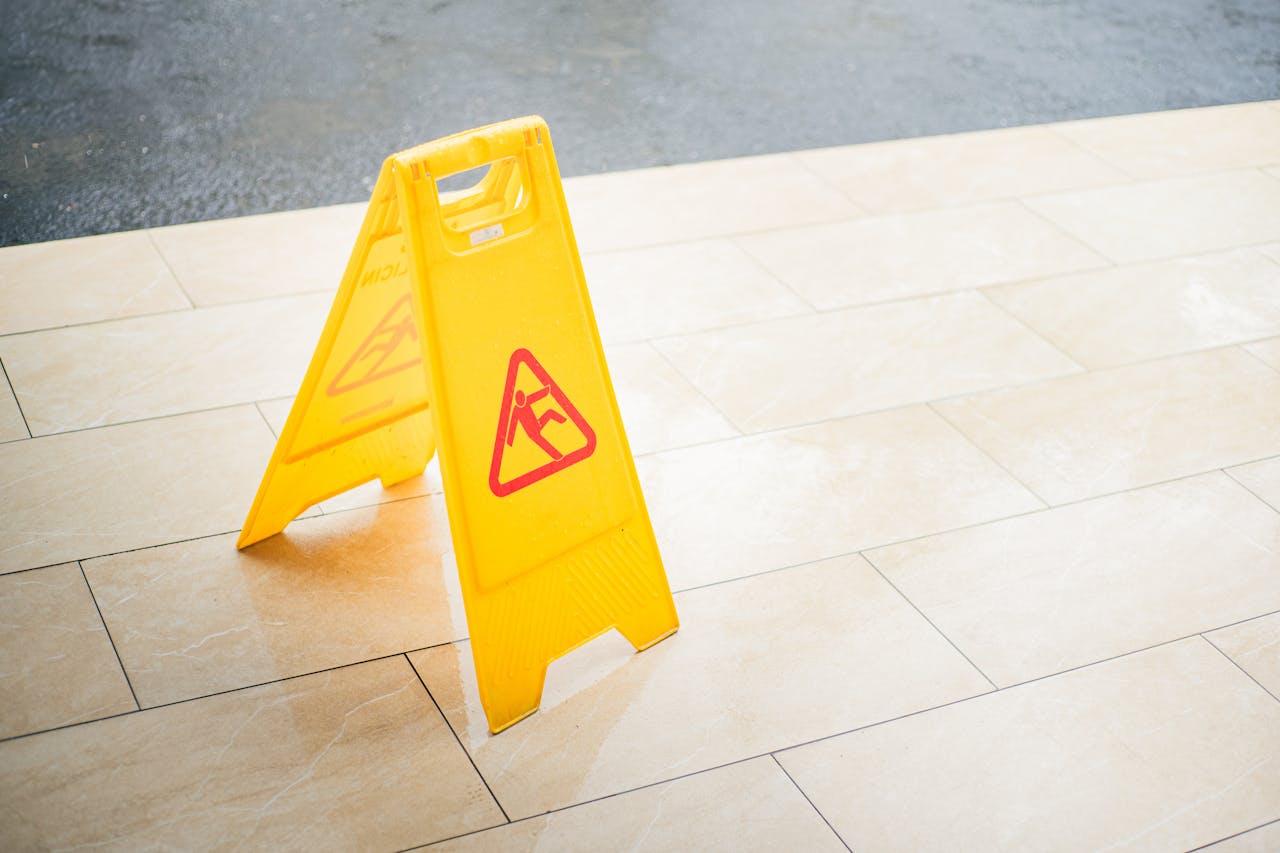 about-01 A bright yellow caution sign placed on a tile floor indicating a wet area for safety.